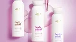 Three Dove Body+Mind serum body wash bottles displayed on a pink background with liquid droplets.