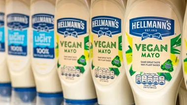 A close-up of Hellmann’s mayonnaise bottles on a shelf, featuring a mix of ‘Light’ and ‘Vegan Mayo’ varieties. The Vegan Mayo bottles are labelled with ‘Same Great Taste, 100% Plant-Based’ and ‘100% Recycled Bottle’.