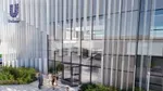 An artist’s impression of a modern office building with a glass facade and vertical white slats. The Unilever logo is visible in the top left corner. Several people are walking or standing near the entrance, which features revolving doors. The surrounding area has landscaped greenery and flowers.