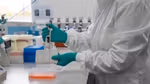 A scientist at work in a Unilever R&D lab. Their face is not visible. They are wearing a white lab coat and green gloves, holding a device.
