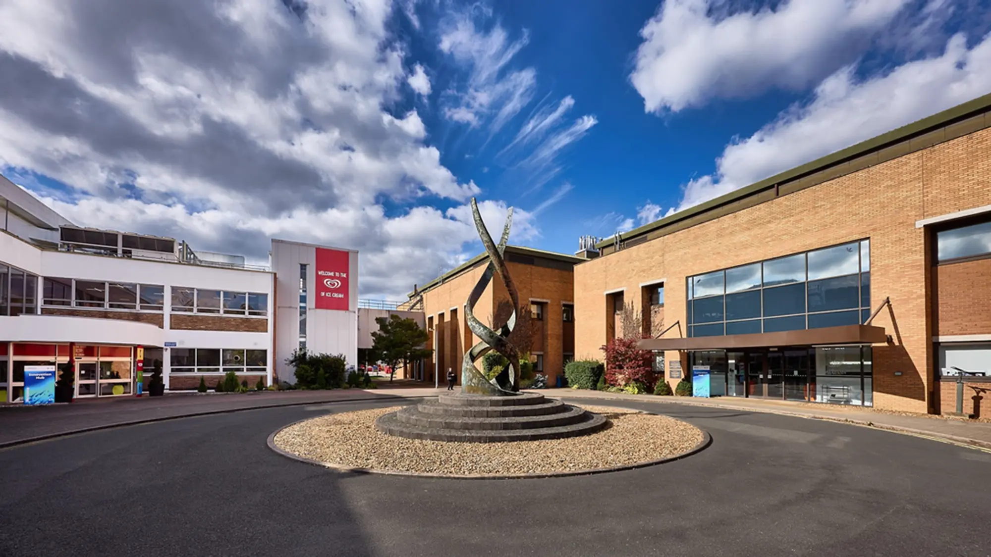 Several low-level office buildings, some white and some red brick, with a circular drive and an ornamental structure in the foreground.