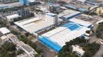 Aerial view of Unilever’s Gandhidham personal care site in India showing interconnected factory buildings with blue roofs, a central multi-storey processing unit with pipes and a chimney, loading bays, storage areas and access roads within a developed site.