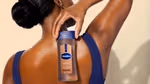Person holding a bottle of Vaseline Cocoa Radiant lotion against their back, wearing a sleeveless top with smooth, moisturized skin.