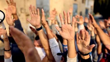 A close-up of a large group of people with their arms raised and palms facing forwards.
