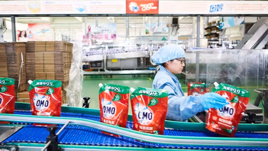 A lady wearing unilever uniform in a factory manning a line producing OMO laundry detergent