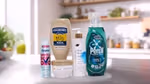 Five household and personal care products displayed on a kitchen counter: a bottle of Hellmann’s Real Mayonnaise, Degree Whole Body Deodorant spray, Dove Intensive Repair cream jar, Dove Pro-Ceramide body serum with pump, and Persil Wonder Wash laundry detergent in a green bottle. A blurred kitchen background with plants and utensils is visible.