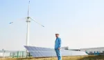 Worker in front of solar panels and wind turbine