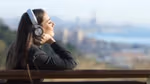 A woman with headphones sitting on bench overlooking a city in the distance