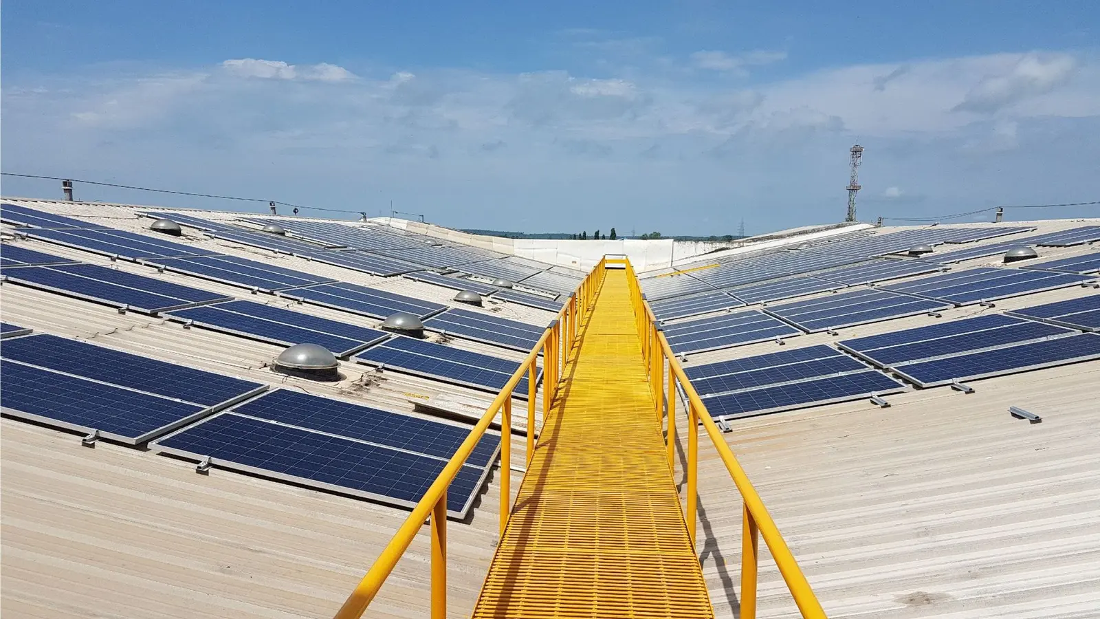 A yellow metal walkway runs through the centre of an array of solar panels on the roof of a Unilever building in India.