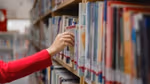 A woman reaching for a book from a full shelf in a library