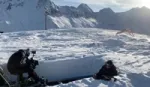 On a sunny snow field surrounded by mountains  a photo crew ski wear is photographing a man doing press-ups in boxer shorts