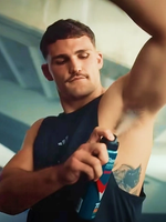A man dressed for the gym confidently applies deodorant to his underarm.