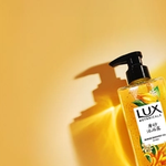 Lux Botanicals Scrub Shower Gel bottle on yellow background.
