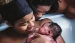 A mother happily cradles her newborn baby in a birthing pool. A man at her side looks on proudly.