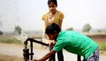 Two children playing and drinking water by an outdoor water tap