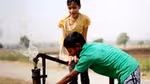 Two children playing and drinking water by an outdoor water tap