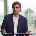 A person wearing a dark blazer and white shirt stands indoors in front of large windows. On-screen text in a blue box reads ‘Fernando Fernandez – Chief Executive Officer.