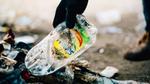 Gloved hand picking up discarded Sunlight plastic bottle from the ground for it to be collected and recycled.