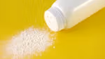 Bottle of talcum powder with some powder on yellow surface