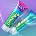 Two Closeup toothpaste tubes on a purple-to-teal gradient background with a splash of water.