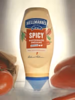 Bottle of Hellmann’s Spicy Mayonnaise Dressing with chili pepper graphics, placed upright on a surface with fresh tomatoes around it.