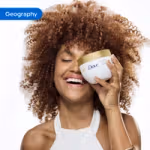 Person holding a Dove body care product in a bathroom setting with white tiles in the background. The image is tagged ‘Geography’.