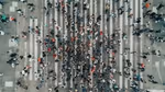 An aerial view of a crowded pedestrian crossing, with numerous people walking in various directions across the striped, white lines.