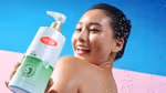 A smiling woman holds Lifebuoy Anti Acne antibacterial body wash -– a white and green bottle with a red Lifebuoy logo.